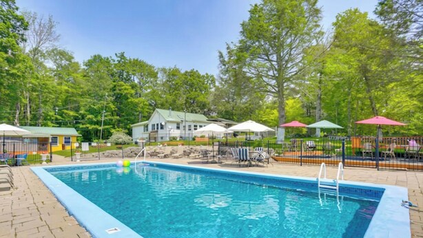 A rectangular swimming pool with a blue edge, surrounded by lounge chairs and umbrellas, with a house and trees in the background. - 5 Mi to Marina & Raceways: Monticello Retreat! (Mongaup Valley)