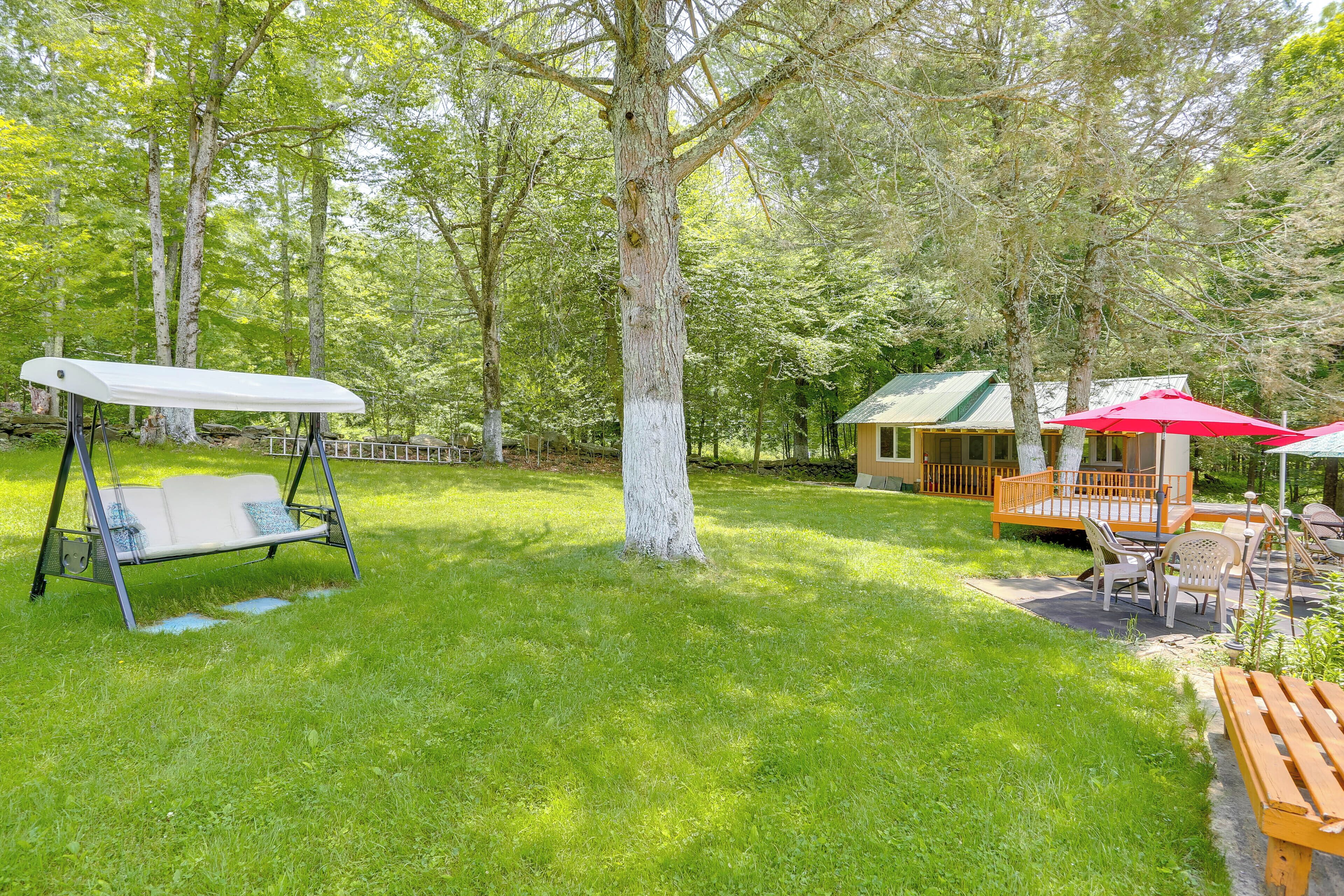 A grassy backyard with a swing set, a wooden deck with outdoor furniture, and a small cabin with a green roof.