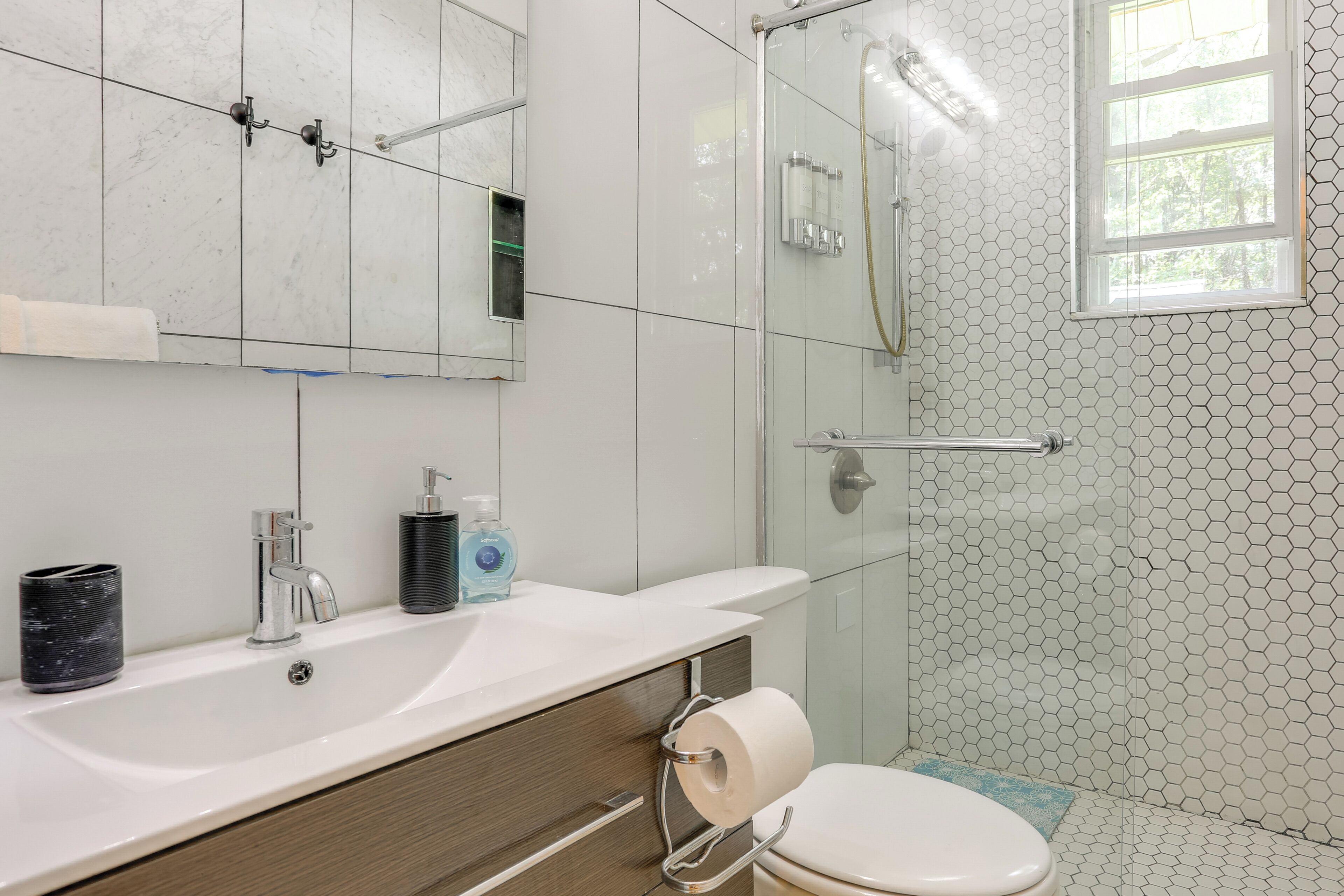 A modern bathroom with a glass shower enclosure, a white sink with a mirror above it, and a toilet with a blue mat.