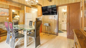 A modern kitchen with wooden walls, a glass dining table, and a flat-screen TV mounted on the wall. - Community Perks: Monticello Cabin w/ Grill! (Mongaup Valley)