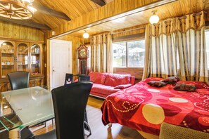 Ein Zimmer mit Holzwänden, einem Glastisch, einem roten Sofa und einem Bett mit einer rot-weißen Bettdecke.