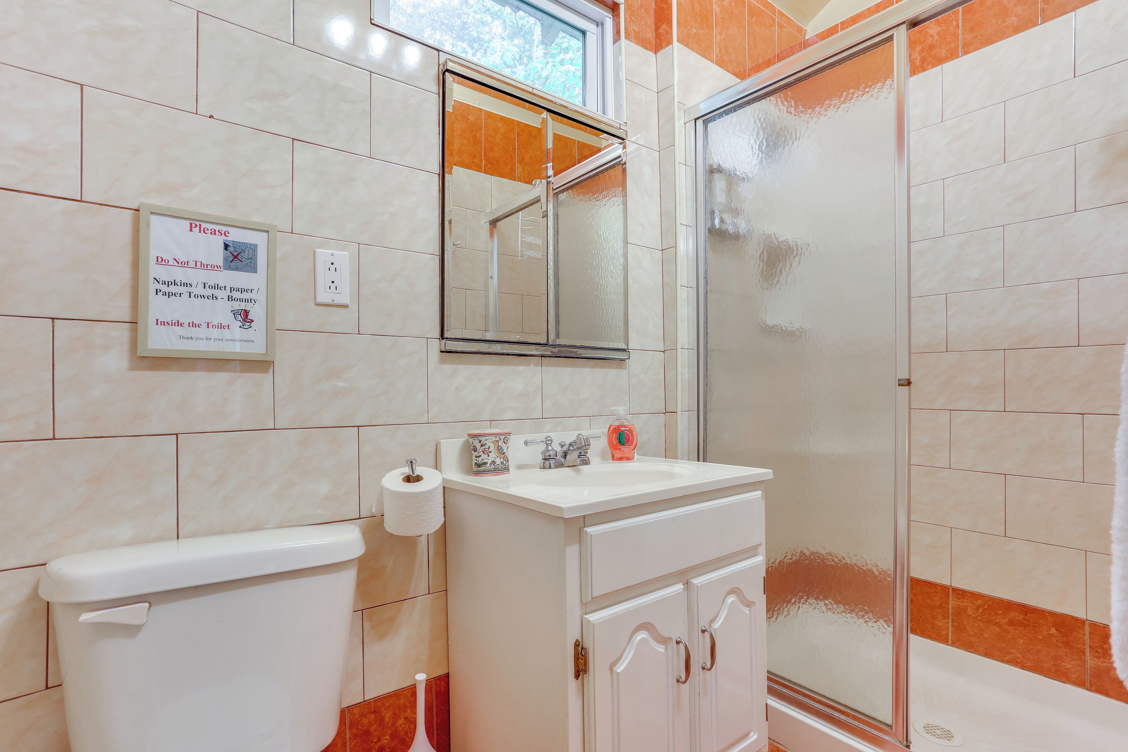 A bathroom with a toilet, sink, and shower. There is a sign on the wall instructing not to throw paper products into the toilet.