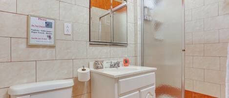Een badkamer met toilet, wastafel en douche. Er hangt een bordje op de muur met de instructie om toiletpapier niet in het toilet te gooien.