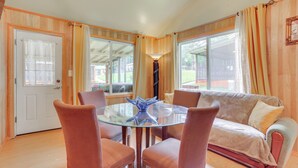 Ein gemütliches Zimmer mit einem Glastisch, umgeben von Stühlen, einer Couch und großen Fenstern mit Vorhängen.