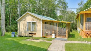 Eine kleine Holzhütte mit Veranda, umgeben von einem grünen Rasen und Bäumen.