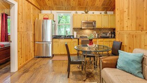 A cozy cabin-style kitchen with wooden walls and a dining area featuring a round glass table and chairs. - 6 Mi to Bethel Woods Center: Cabin Near Shops (Mongaup Valley)