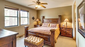 A bedroom with a large bed, two bedside tables, a wooden dresser, a tufted ottoman, a ceiling fan, and two windows. - 4 Miles to Lake: Retreat w/ 2 Decks! (Show Low)