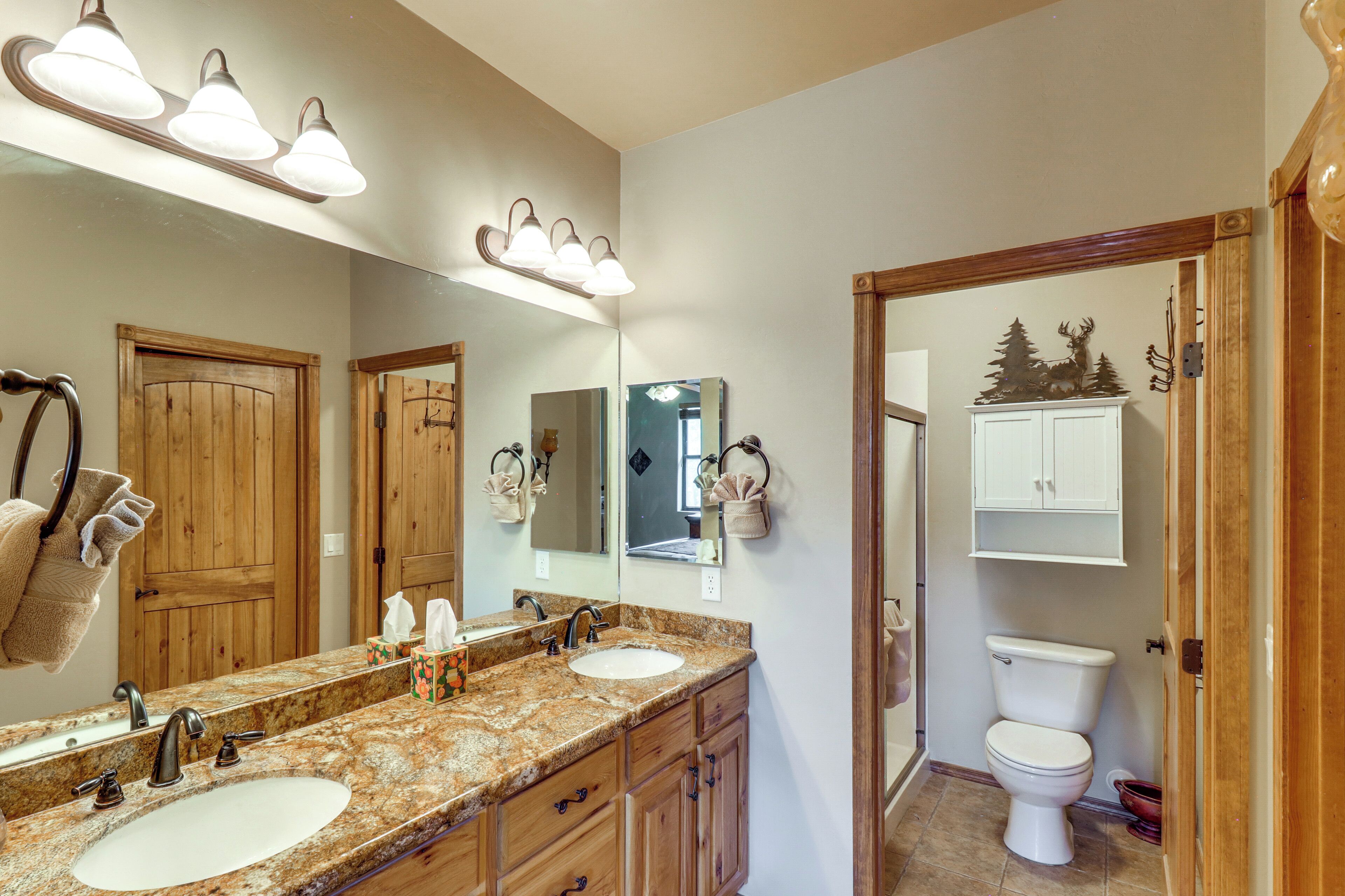 A bathroom with a double sink, wooden cabinets, a large mirror, and a toilet.