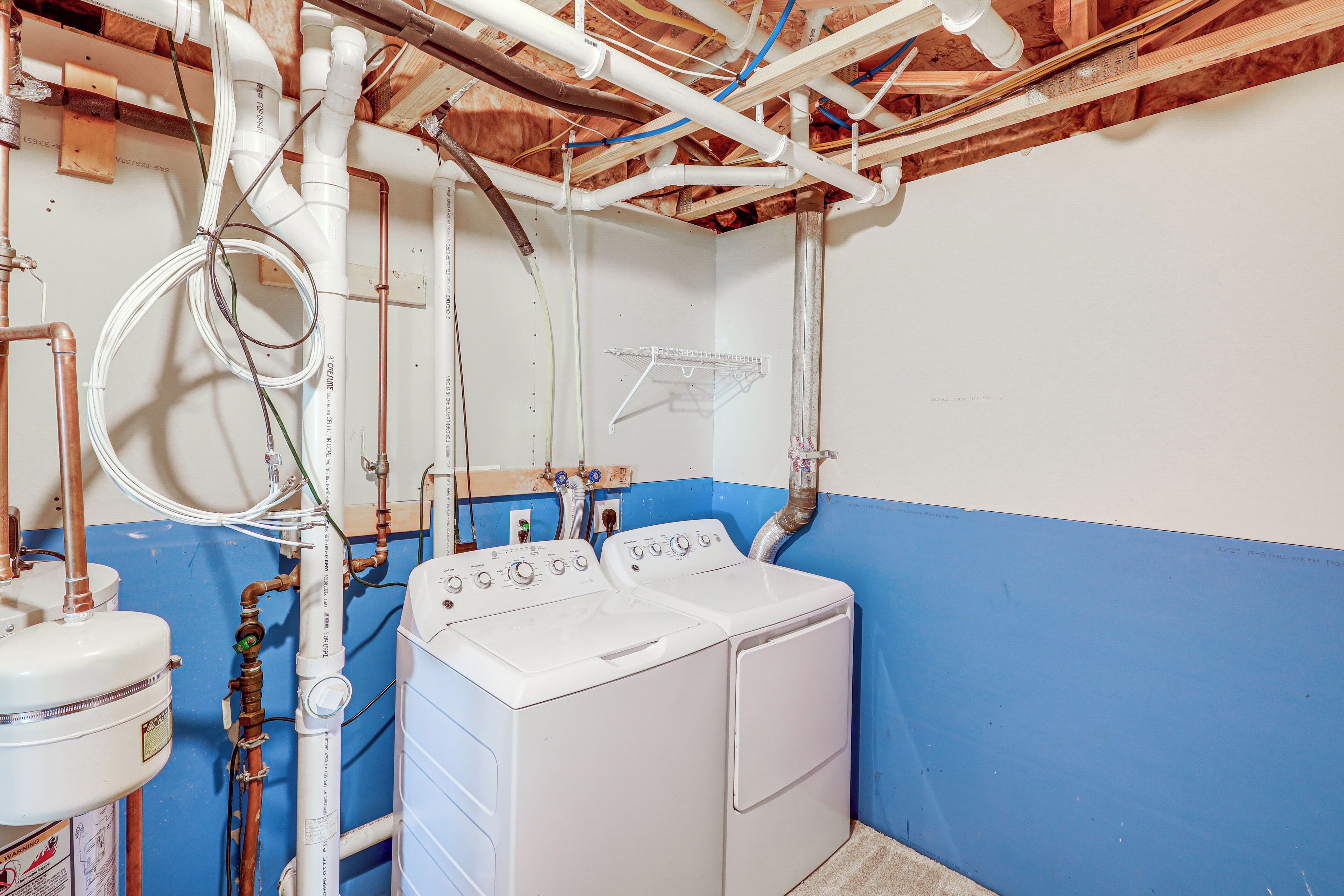 Une buanderie avec deux machines à laver et deux sèche-linge blancs, des tuyaux apparents et un mur bleu.
