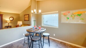 A dining area with a round table, four stools, a chandelier, a world map, and a window with blinds. - 4 Mi to Offutt AFB - Family Home in Omaha Suburbs! (Bellevue)