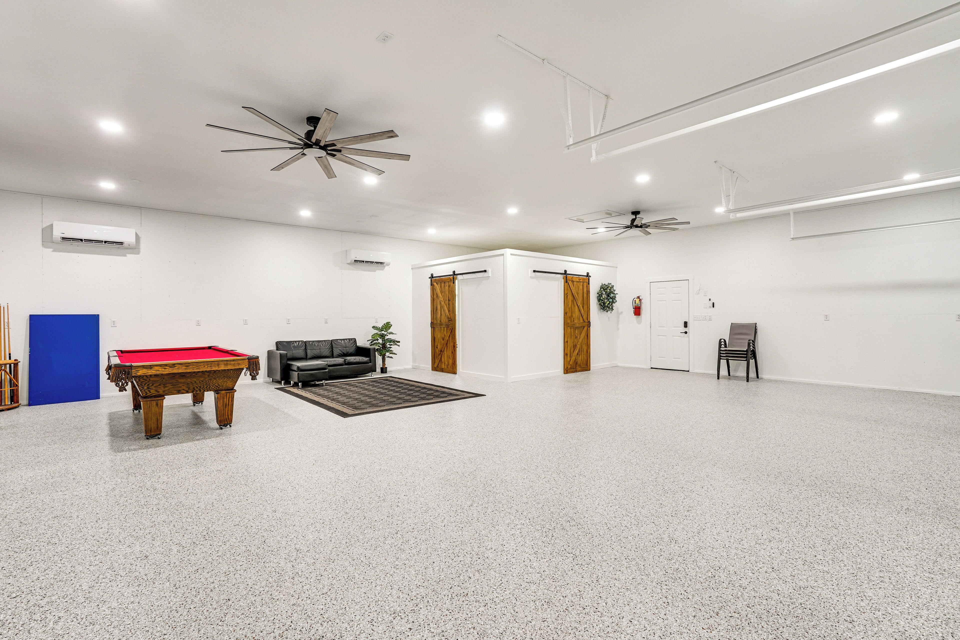 A spacious indoor area with a pool table, a sofa, and a ceiling fan.
