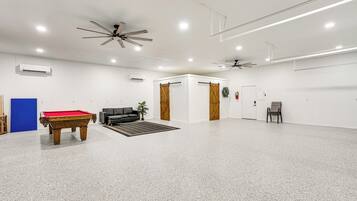 A spacious indoor area with a pool table, a sofa, and a ceiling fan.