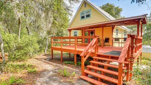 A yellow house with a wooden deck and stairs leading to a porch. - Walk to Lake George: Quiet Nature Escape w/ Deck (Fort McCoy)
