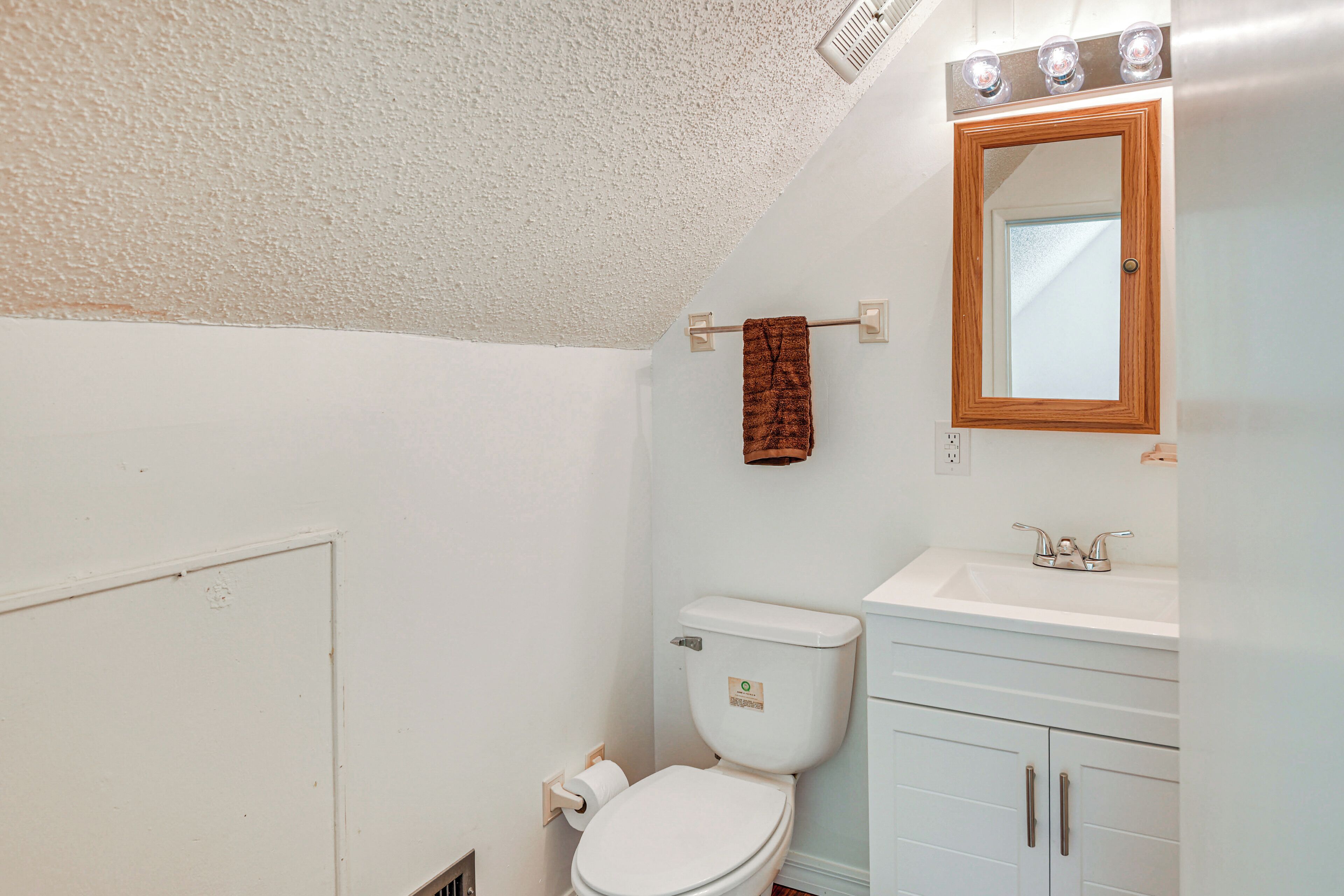 A bathroom with a white toilet, a sink with a mirror, and a towel hanging on a rack.
