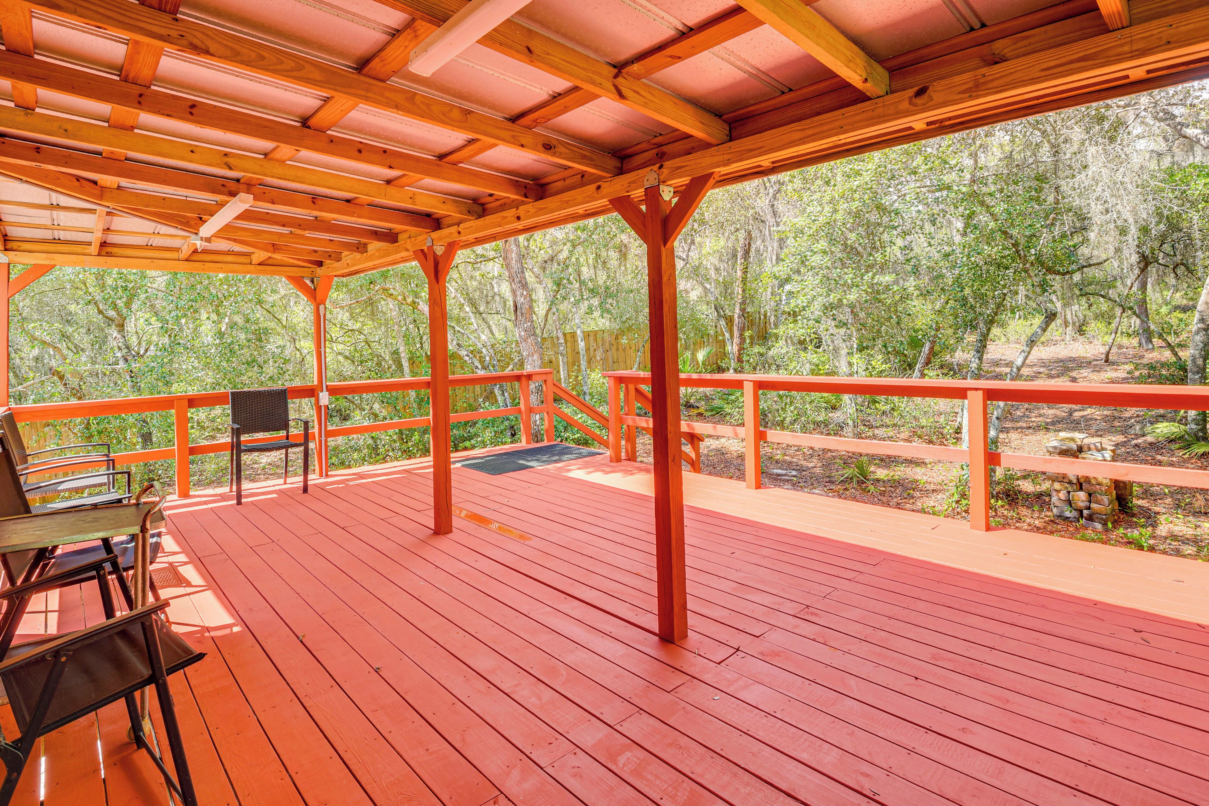 Terraza de madera al aire libre con barandas rojas y bancos, rodeada de árboles.
