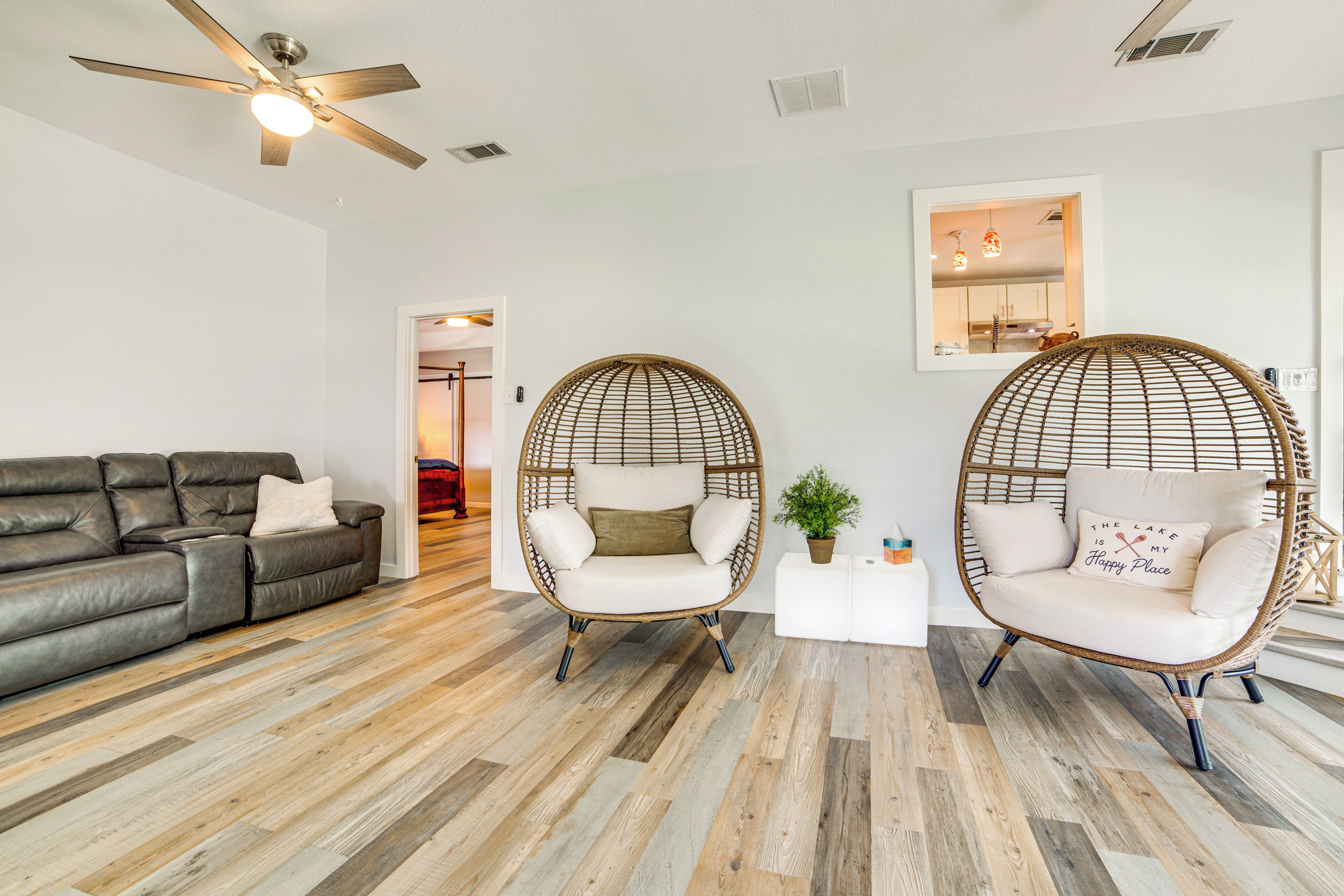 A modern living room with a grey leather sofa, two wicker armchairs, a white coffee table, and a ceiling fan.