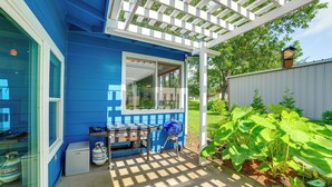 Una casa azul con un porche cubierto, una parrilla y un jardín con plantas de hojas grandes.
