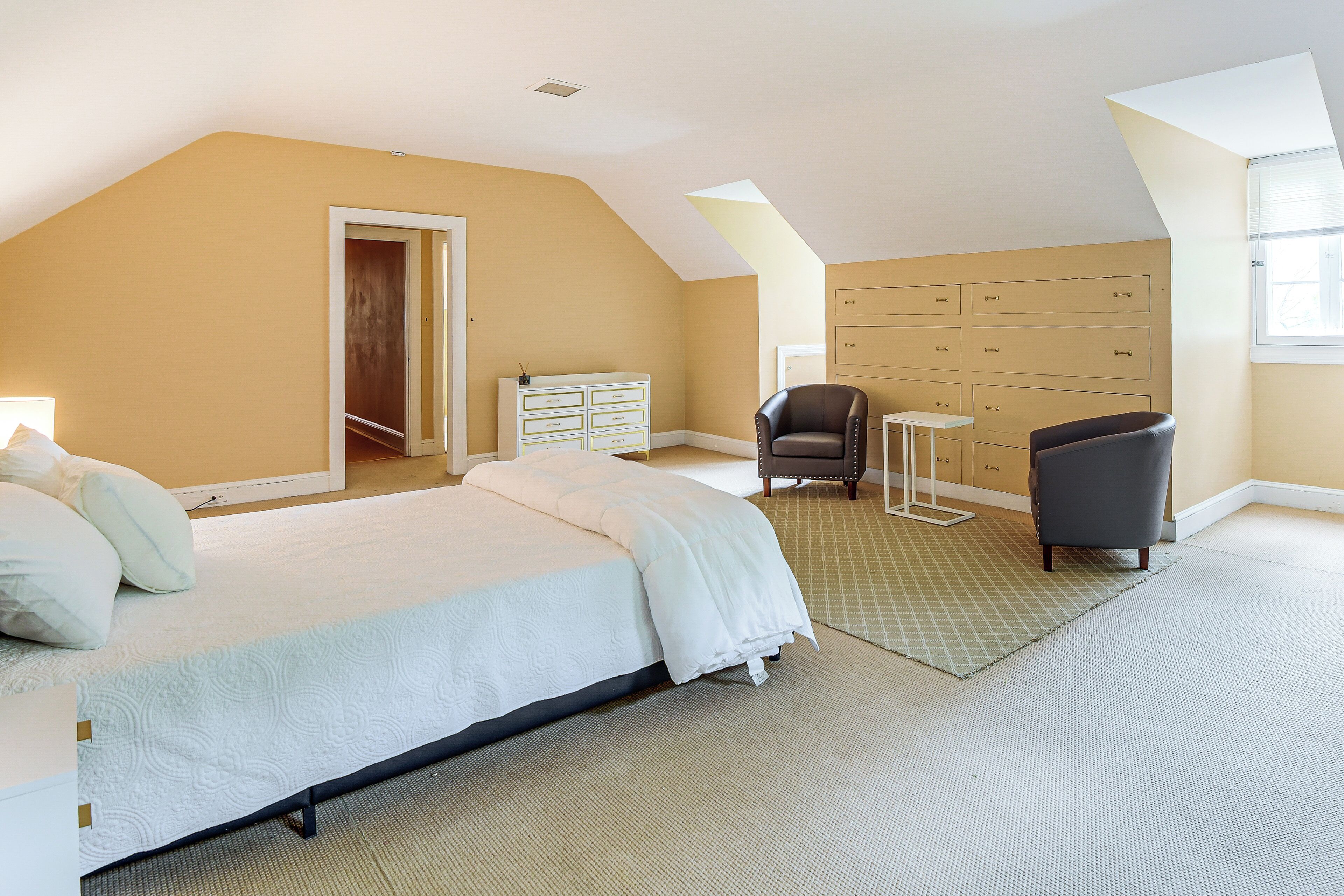 A bedroom with a bed, two chairs, a dresser, and a window.