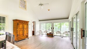 A spacious room with hardwood flooring, a wooden cabinet, a ceiling fan, and large windows offering a view of greenery outside. - Near Shops & Parks: Dog-friendly Maryland Gem (Owings Mills)