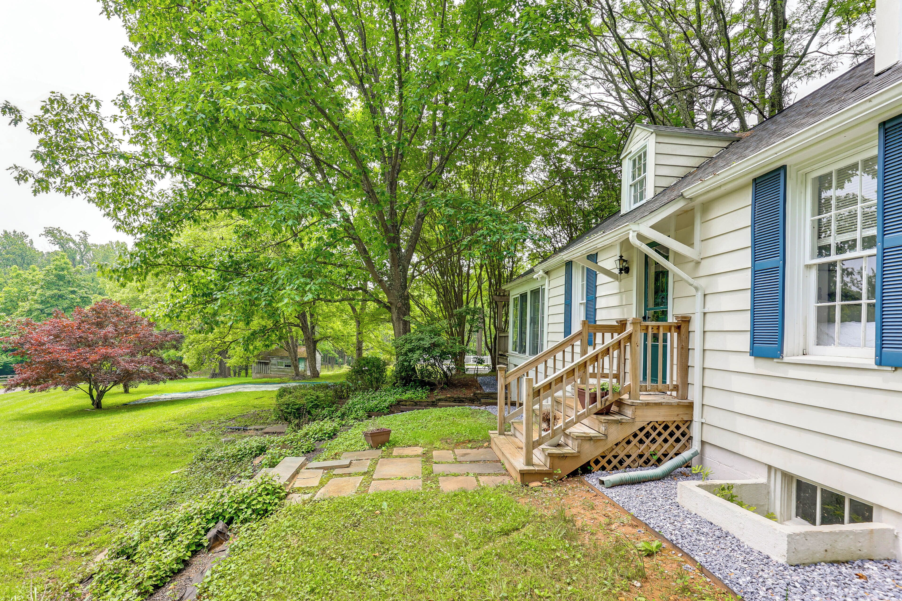 A house with a wooden staircase leading to a porch, surrounded by a well-maintained garden and trees.