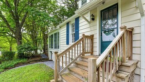 A wooden staircase leading to a front door with blue shutters, surrounded by a garden and trees. - Near Shops & Parks: Dog-friendly Maryland Gem (Owings Mills)