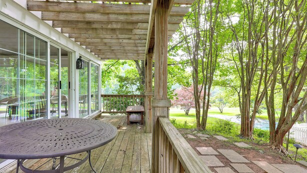 A wooden deck with a round table and chairs, surrounded by glass doors and a view of trees and a garden. - Near Shops & Parks: Dog-friendly Maryland Gem (Owings Mills)