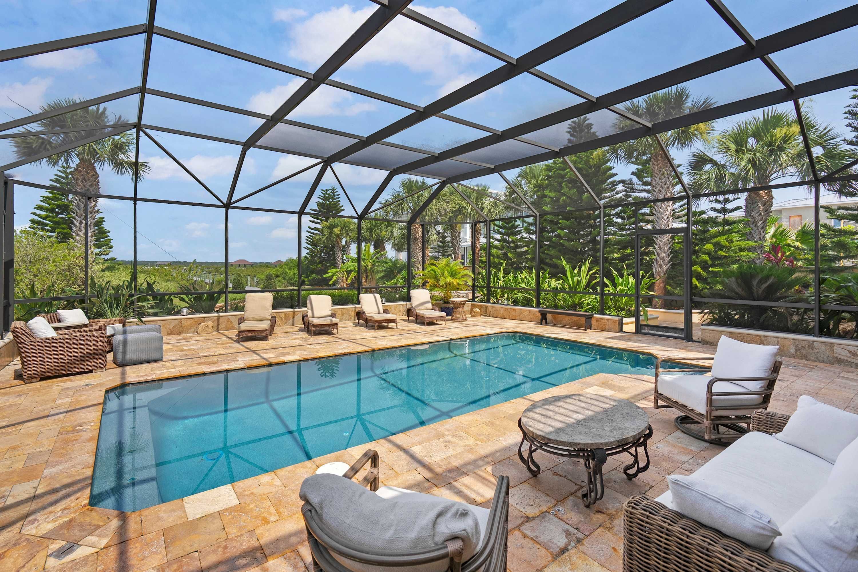 Piscina exterior techada con sillas de descanso y una mesa, rodeada de follaje.
