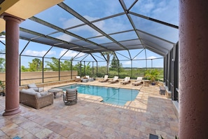A covered outdoor swimming pool area with lounge chairs and a wicker sofa.