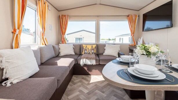 A cozy living room with a sofa, a dining table set for two, and large windows with curtains. - 3 Bedroom Caravan-seton Sands (Prestonpans)