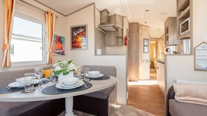 A dining area with a table set for four, a kitchen with wooden cabinets, and a view of the beach through the window. - 3 Bedroom Caravan-seton Sands (Prestonpans)
