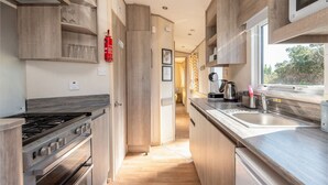 A modern kitchen with wooden cabinets, a stainless steel stove, and a large window providing natural light. - 3 Bedroom Caravan-seton Sands (Prestonpans)