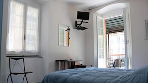 Une chambre à coucher comprenant un lit, un bureau, une chaise, un téléviseur fixé au mur et une fenêtre avec des rideaux.