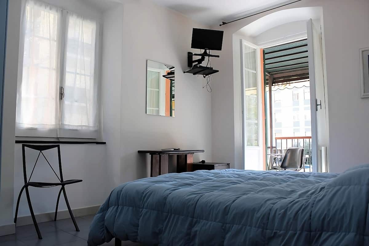 A bedroom with a bed, a desk, a chair, a TV mounted on the wall, and a window with curtains.