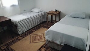 A small, clean room with two single beds, a small wooden table, and a patterned rug.
