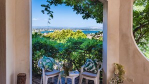 Un espace extérieur aménagé avec deux chaises et une table, offrant une vue panoramique sur un paysage côtier verdoyant, avec des arbres et une étendue d’eau.