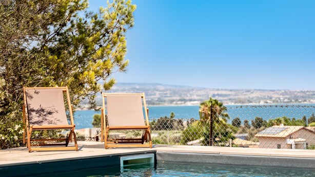 Un espace aménagé au bord de la piscine, avec deux chaises longues en bois et une vue sur la mer.