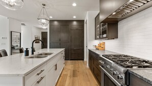 A modern kitchen with a central island, stainless steel appliances, and a wooden floor. - The Yucca Flower #11: Dog Friendly + Luxury Home (Ivins)