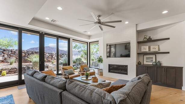 A modern living room with a gray sectional sofa, a fireplace, and a large window offering a view of a rocky landscape. - The Yucca Flower #11: Dog Friendly + Luxury Home (Ivins)