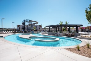 A swimming pool with a spiral slide, lounge chairs, and a covered seating area.