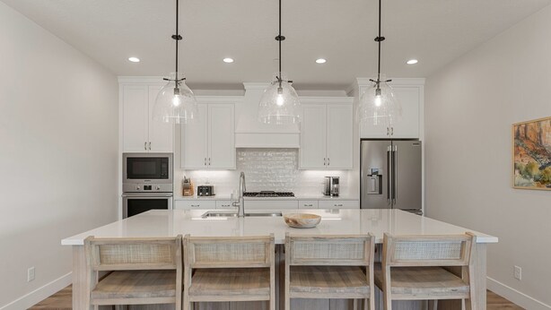 A modern kitchen with white cabinetry, a large island, and three pendant lights.