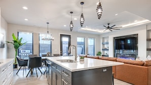 Cocina moderna con una isla central, electrodomésticos de acero inoxidable y una zona de estar con sofá de cuero marrón.