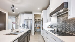 Una cocina moderna con armarios blancos, electrodomésticos de acero inoxidable y un salpicadero de baldosas en patrón de espiga.