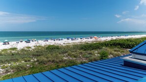 A beach with white sand and clear blue water. There are umbrellas and people on the beach.