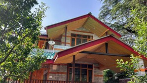 A two-story building with a balcony, large windows, and a red and green exterior. - MonAmis Home (Manali)