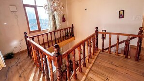 A wooden staircase with a chandelier, a window with curtains, and a framed picture on the wall. - MonAmis Home (Manali)