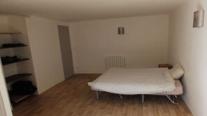 Une petite pièce, peu meublée, avec un lit simple, un radiateur et une armoire.