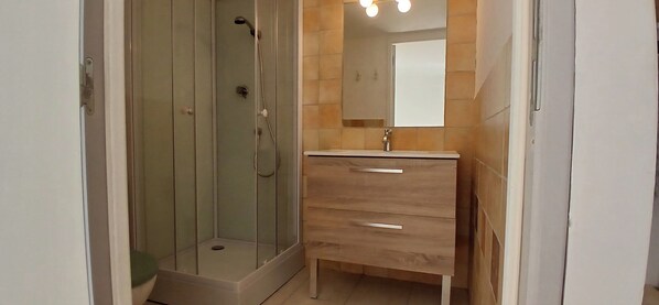 A bathroom with a glass-enclosed shower, a wooden vanity with a mirror, and a tiled floor.