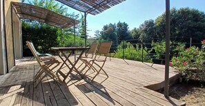 A wooden deck with a table and chairs, surrounded by a metal fence and greenery.