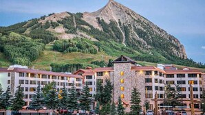 Ein mehrstöckiges Hotel mit einem Steinturm, umgeben von Bäumen und einem Berg im Hintergrund.