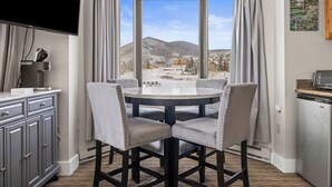 Un comedor con una mesa redonda y cuatro sillas, un televisor montado en la pared, y vistas a un paisaje nevado a través de amplios ventanales.